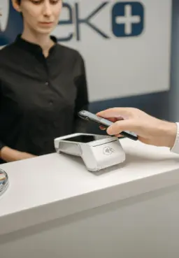 Conseillère en tenue professionnelle assistant un client sur un terminal de paiement, symbolisant le support technique 7j/7 et 24h/24