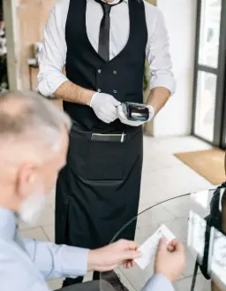 Serveur en tenue professionnelle utilisant un terminal de paiement portable, illustrant un usage multi-secteur pour la collecte de dons et la gestion des pourboires