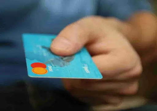 Main tenant une carte Mastercard bleue, symbolisant le paiement au taux bancaire de 0,3% sans commission ni abonnement avec un TPE en achat direct