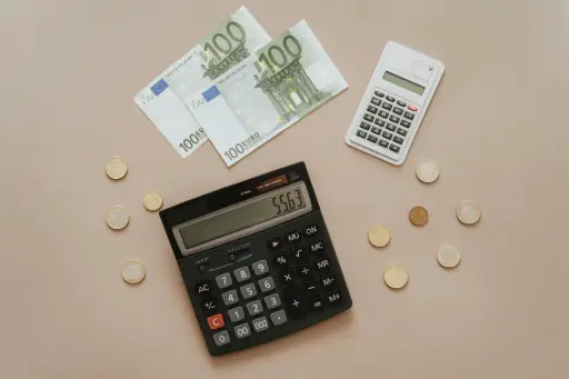 Billets de 100 euros, pièces et calculatrice sur un bureau, illustrant les pertes financières subies par un commerçant victime d'un échange frauduleux de TPE