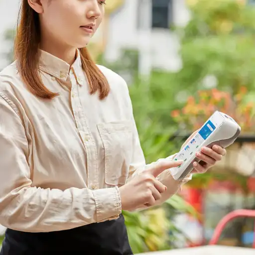 Cette image, mettant en scène une serveuse utilisant le terminal en extérieur, illustre parfaitement la force du PAX A920 Pro : sa mobilité. En tant que solution mobile complète, il est l'outil idéal pour de nombreux secteurs d'activité. Dans la restauration et l'hôtellerie, il permet l'encaissement à table, la gestion des pourboires et des titres-restaurant en toute fluidité. Pour le commerce de détail, il se transforme en caisse mobile lors des pics d'affluence, permet le paiement en rayon et facilite la gestion des stocks grâce à son scanner intégré. Enfin, il est indispensable pour les professionnels en déplacement (artisans, livreurs, taxis) qui ont besoin d'encaisser de manière fiable et sécurisée partout, grâce à sa connectivité 4G. Dans chaque cas, le PAX A920 Pro est l'outil parfait pour moderniser son service et offrir une expérience client irréprochable.