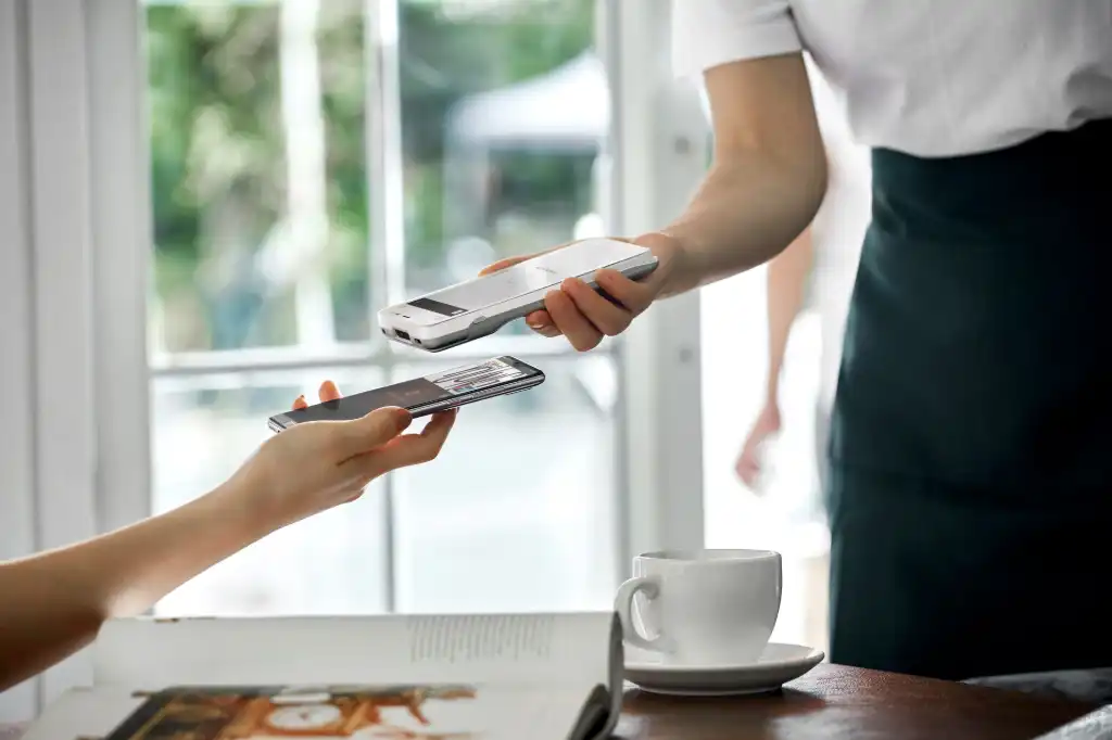 Photo illustrant un paiement en sans contact réalisé avec le terminal de paiement PAX A77 dans un café. Paiement sans contact par paiement mobile avec téléphone portable
